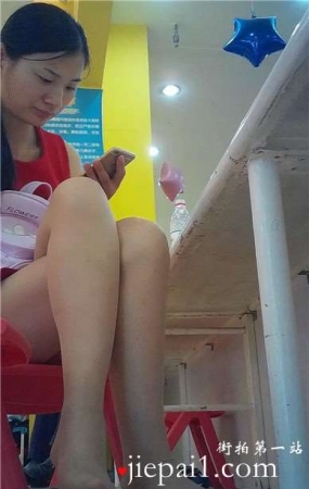 边玩手机边挑些等孩子玩蹦蹦床的红衣少f